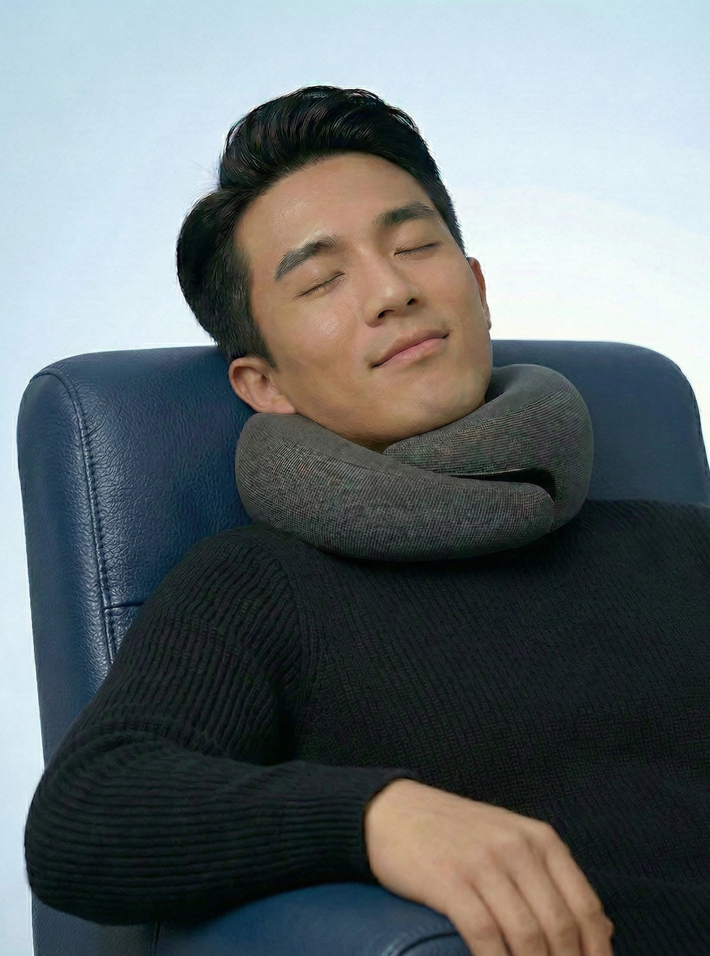 Man using a neck pillow in a chair with a light blue background, spaceblack