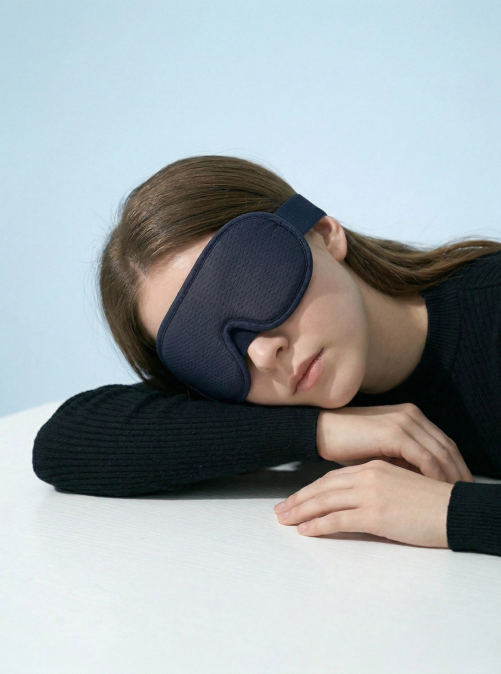 Person wearing a navy blue sleep mask against a light blue background, eclipseblue