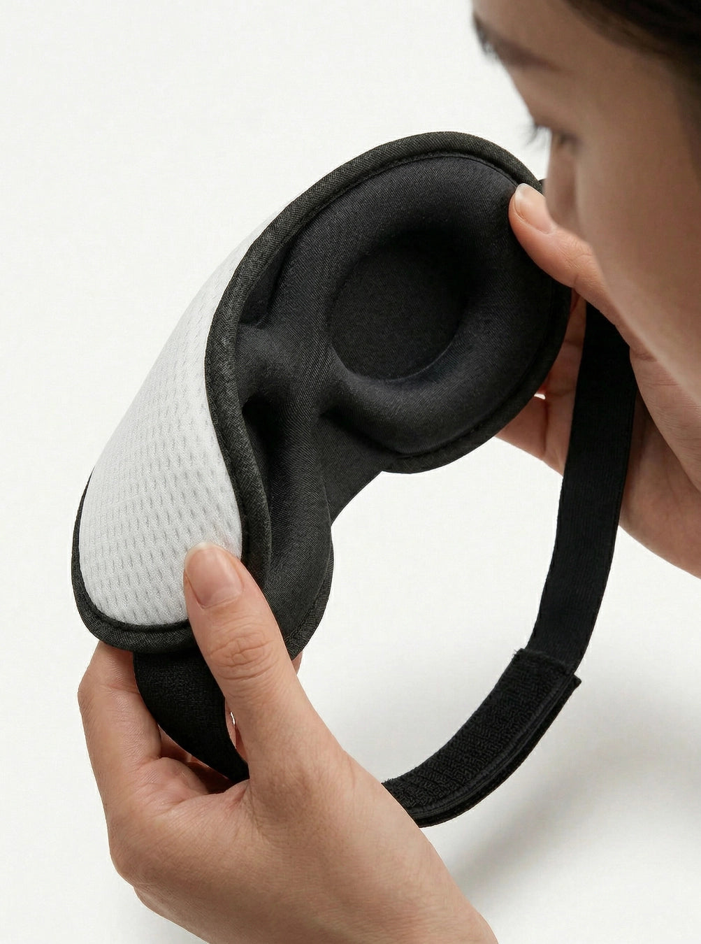 Person holding a black and white eye mask against a light background, cloudwhite