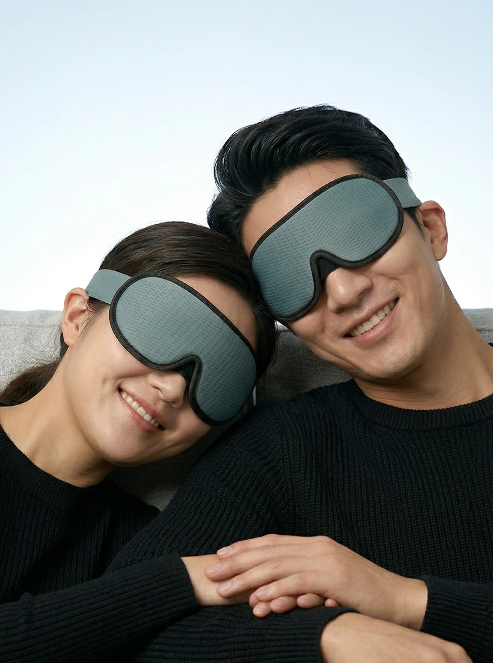 Two people wearing gray sleep masks against a light blue background, dusk