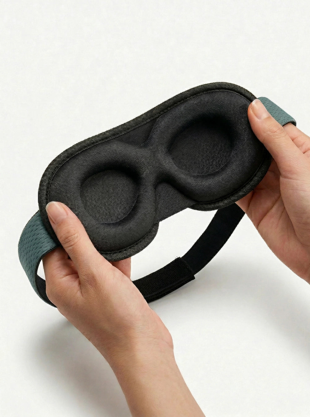 Black sleep mask with gray headband held by hands on a white background, dusk