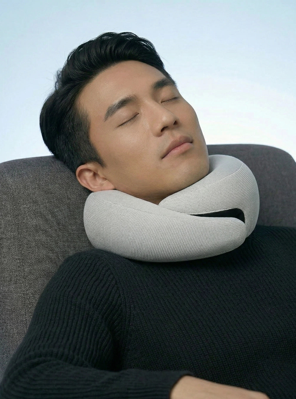 Man using a neck pillow in a chair with a light blue background, stormgrey