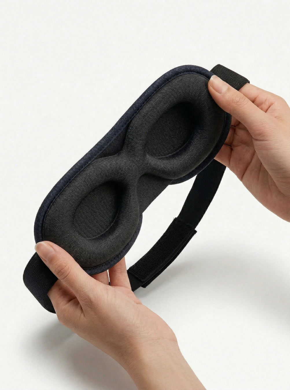 Black sleep mask held by hands on a white background, eclipseblue