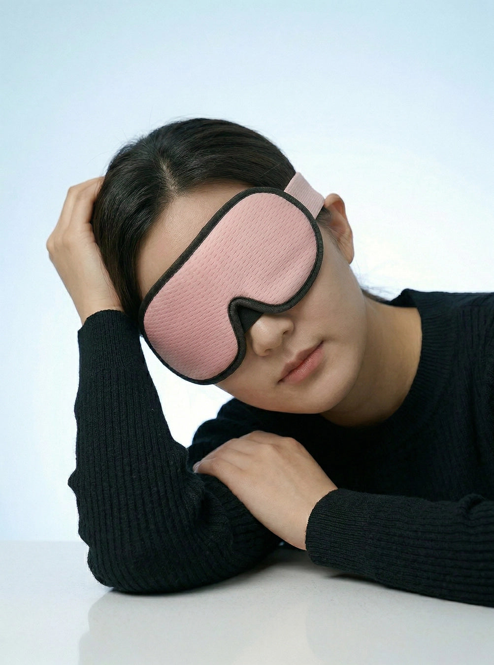 Person wearing a pink sleep mask against a light blue background, peach