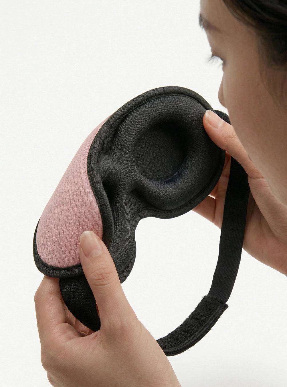 Person holding a black and pink ear muffs against a white background, peach