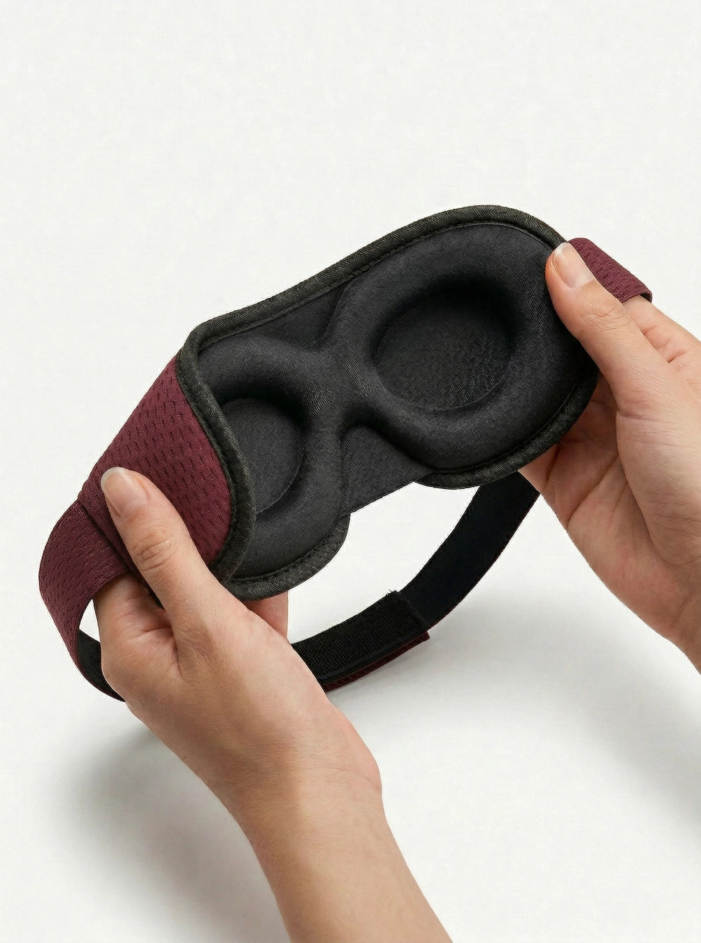 Black sleep mask with red straps held by a hand on a white background, maroon