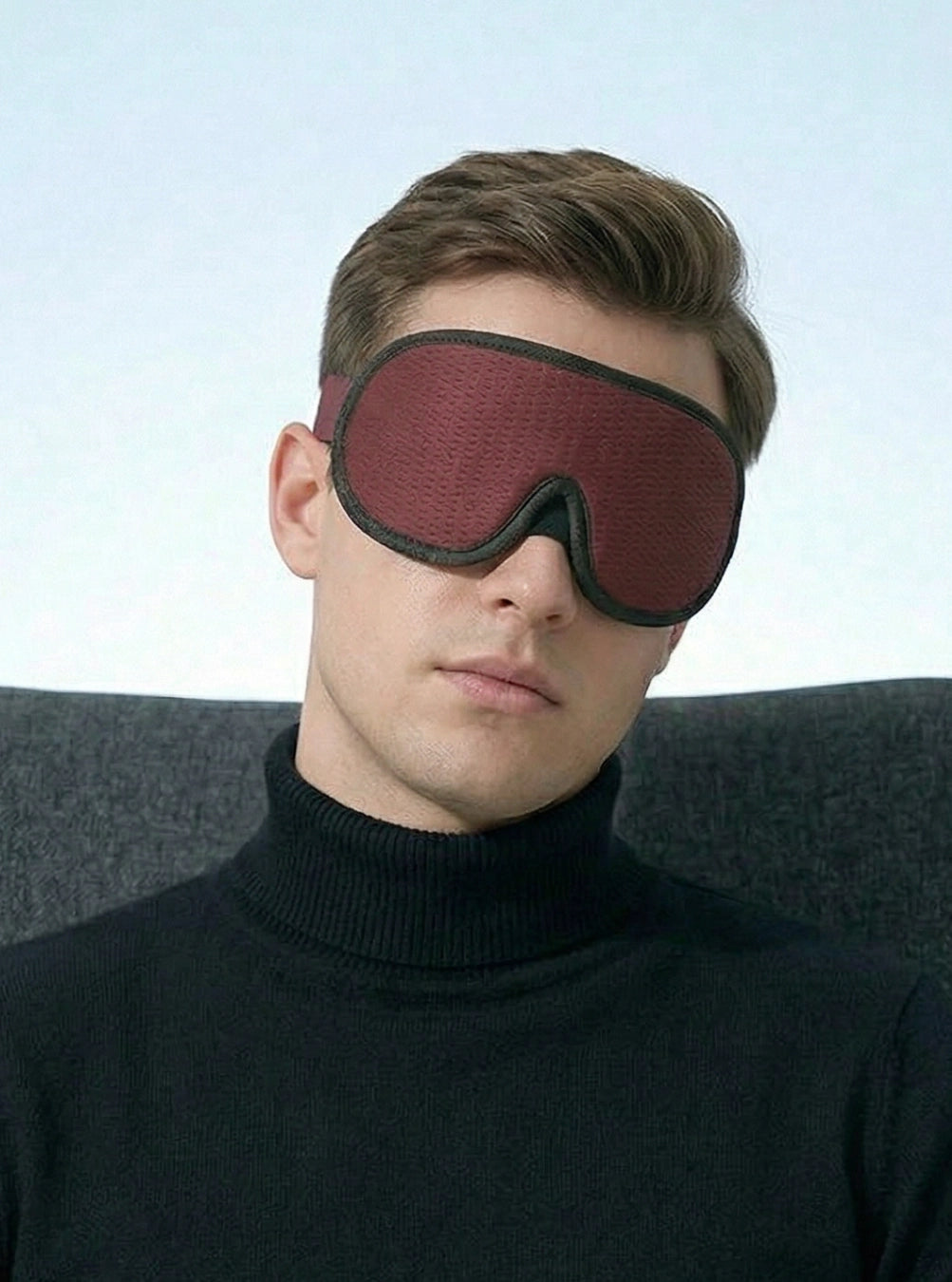 Man wearing a dark red sleep mask against a light blue background, maroon