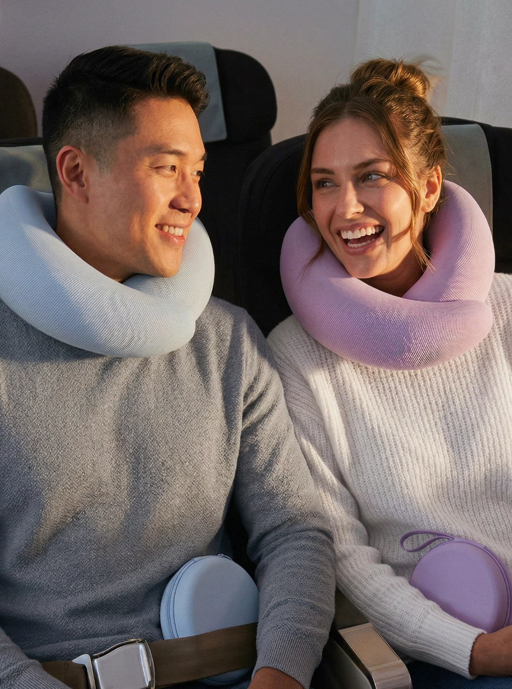 Two people sitting in an airplane with neck pillows, smiling. Skyblue & Lavender