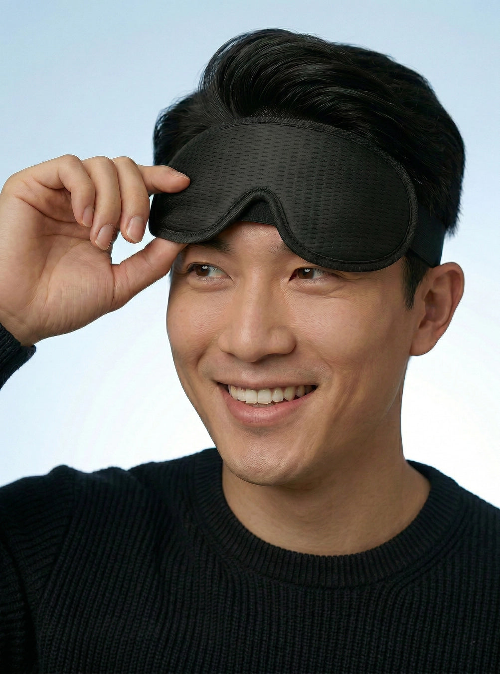 Man holding a black sleep mask against his face on a light blue background, spaceblack