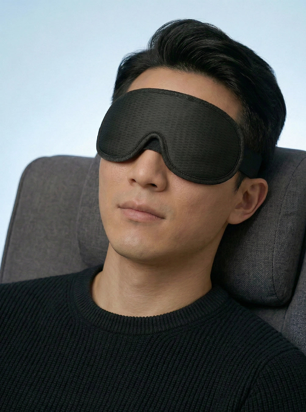 Man wearing a black sleep mask in a chair with a plain background, spaceblack