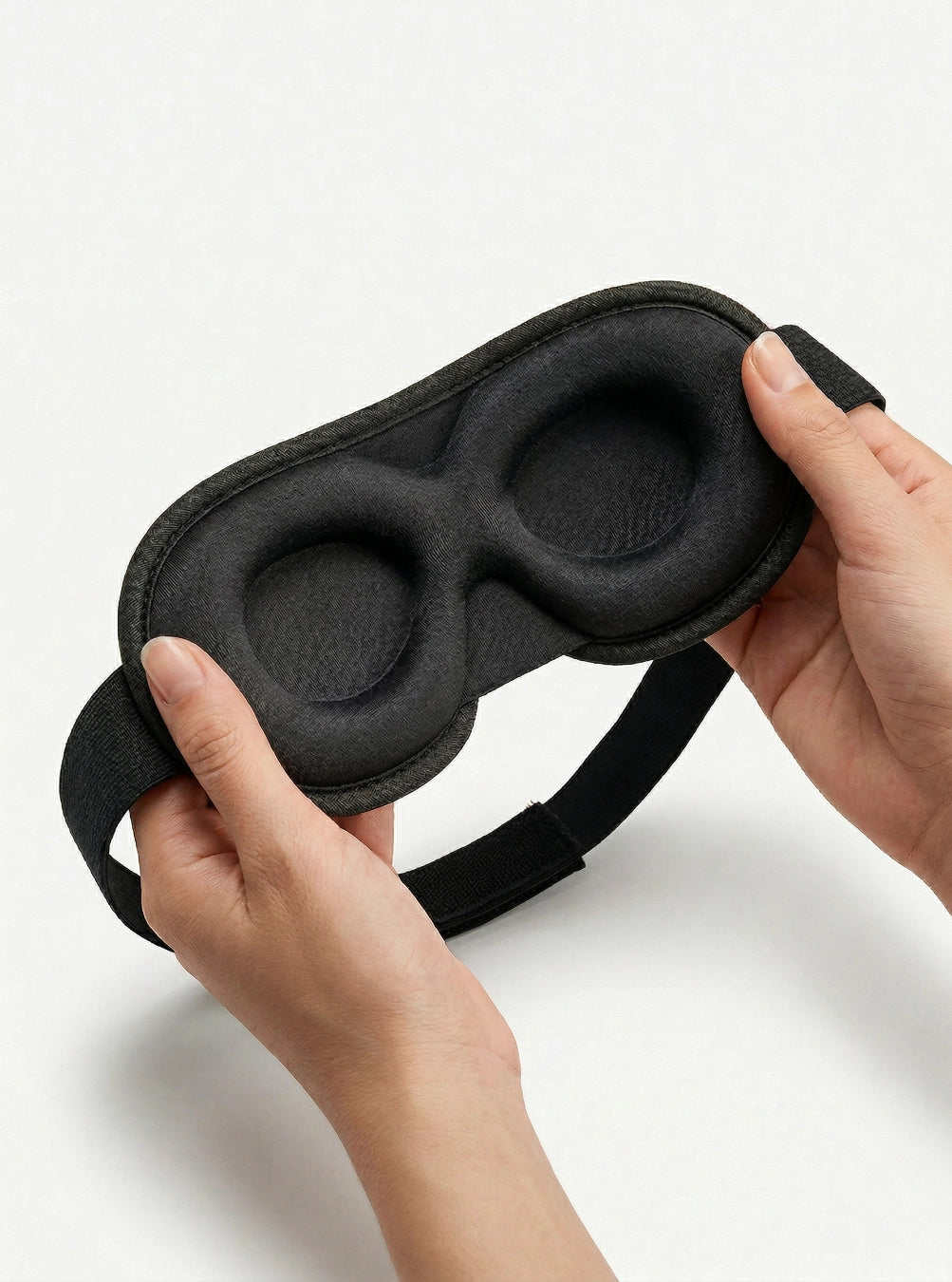 Black sleep mask held by a hand on a white background, spaceblack